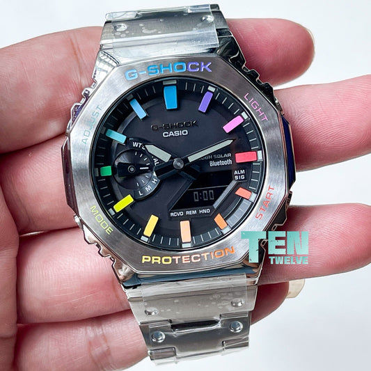 A CasiOak G-Shock stainless steel watch with a silver rainbow-colored bezel, held in a person's hand.