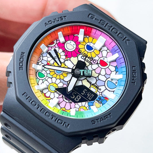 A customized G-Shock CasiOak watch with a black band and a colorful sunflower patterned dial, featuring numbers from 0 to 9, a date display, and the word 'PROTECTION' on the side.