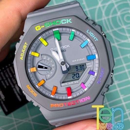 A hand-painted Casio G-Shock watch with colorful hour markers and text on the bezel, predominantly grey with rainbow-colored details.