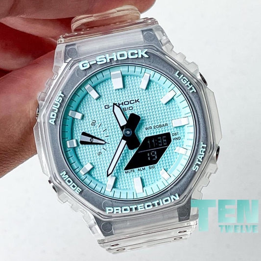 A hand holding a turquoise blue G-Shock wristwatch with a jellyfish design on the band and dial.