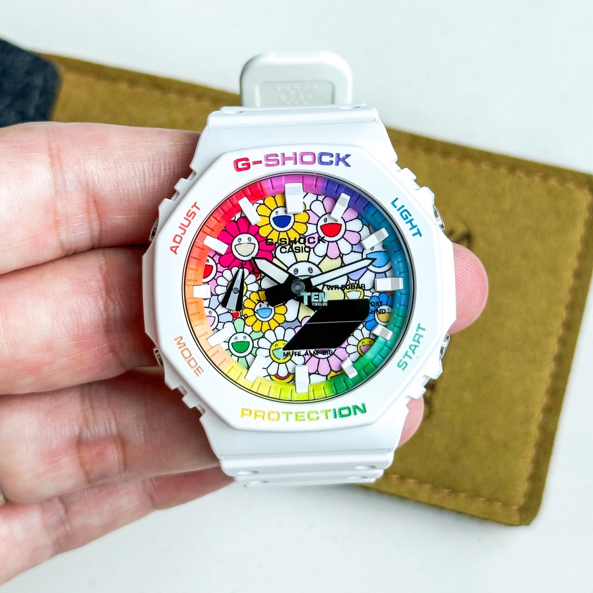 G-Shock watch with colorful face held in a hand on a white background